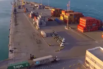 Vista aérea do terminal portuário de Fortaleza com contêineres coloridos, guindastes e caminhões de carga à beira-mar