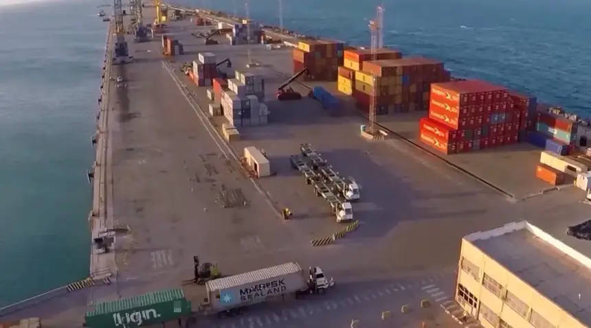 Vista aérea do terminal portuário de Fortaleza com contêineres coloridos, guindastes e caminhões de carga à beira-mar