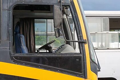 Vista lateral da cabine de um ônibus preto e amarelo, com outro ônibus branco ao fundo