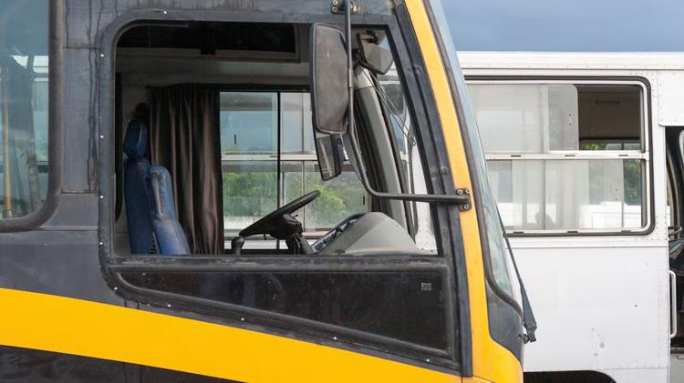 Vista lateral da cabine de um ônibus preto e amarelo, com outro ônibus branco ao fundo